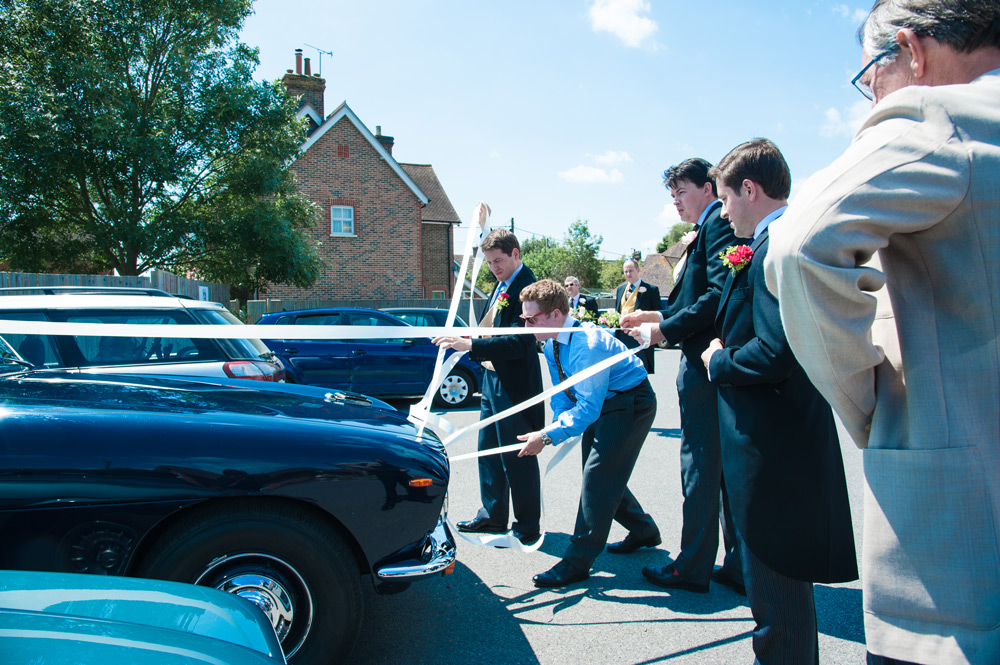 Groomsmen putting wedding ribbon on car