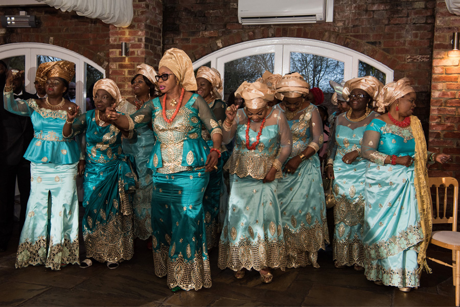 Women in coordinated teal asoebi dancing together at an African-British wedding reception