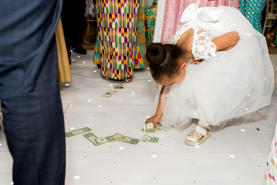 Young girl in a white dress picking up money from the dance floor during an African-British wedding reception