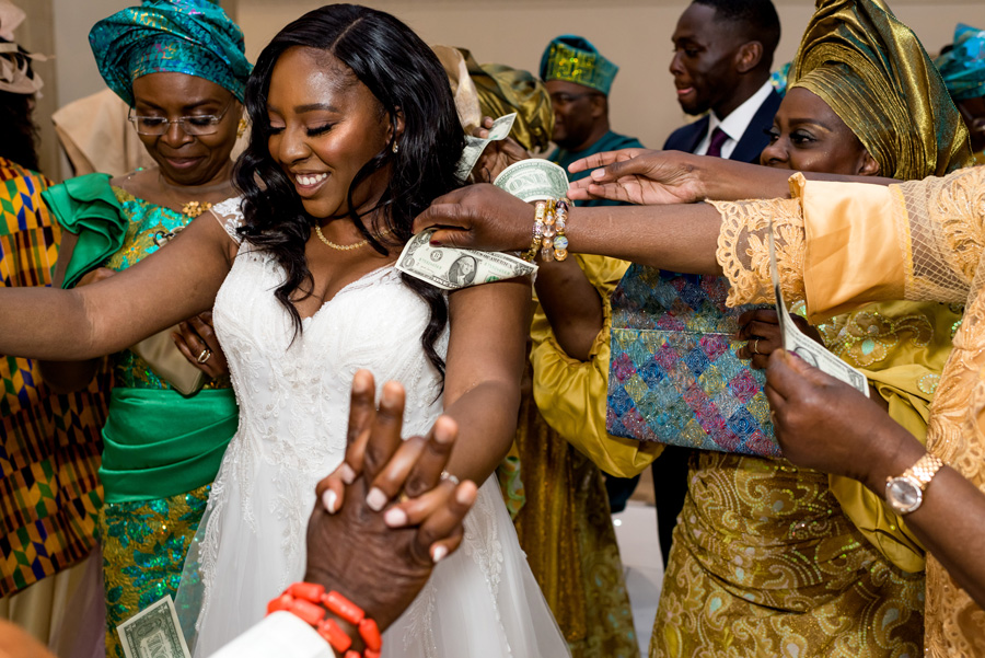 Bride surrounded by female relatives adjusting her jewellery during an African-British wedding celebration