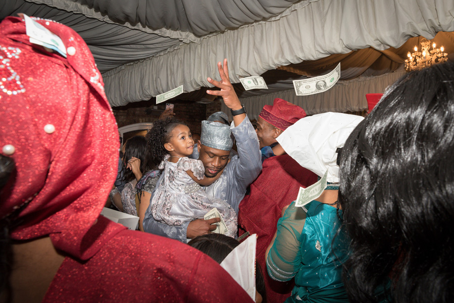 Guests throwing money in celebration on a crowded dance floor at an African-British wedding