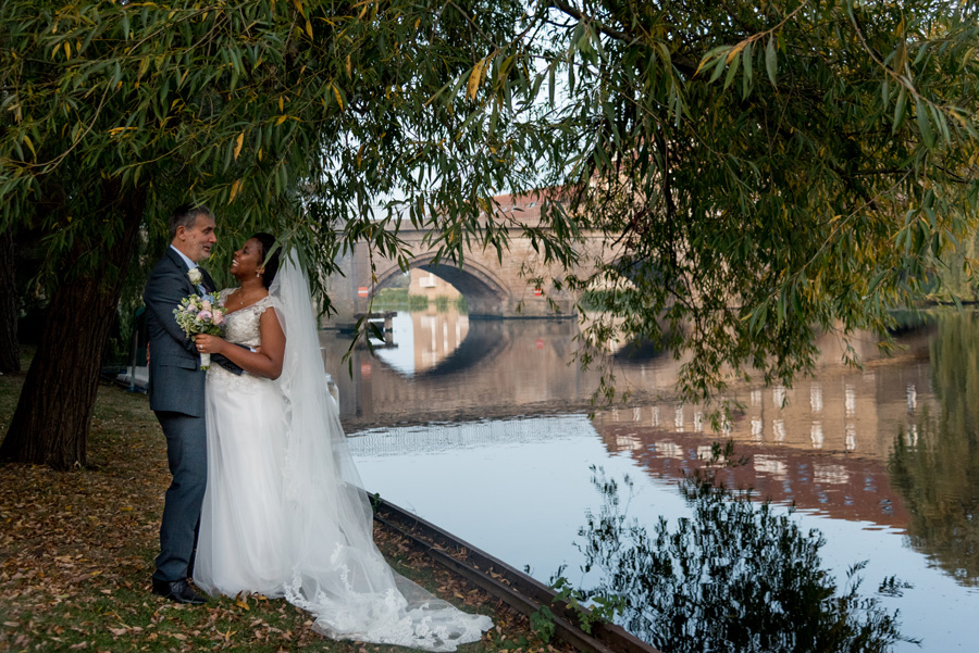 Couple standing by the River Great Ouse near The Old Bridge Hotel in Huntingdon during an autumn wedding portrait