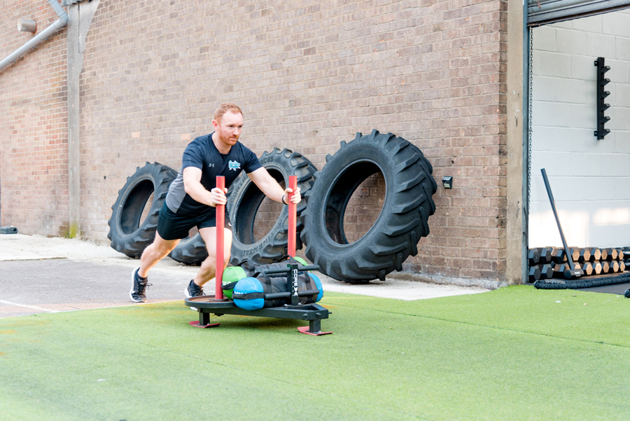 Personal trainer pushes a prowler across grass