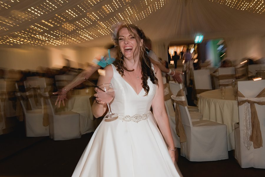 Bride dancing on dancefloor with drink in hand