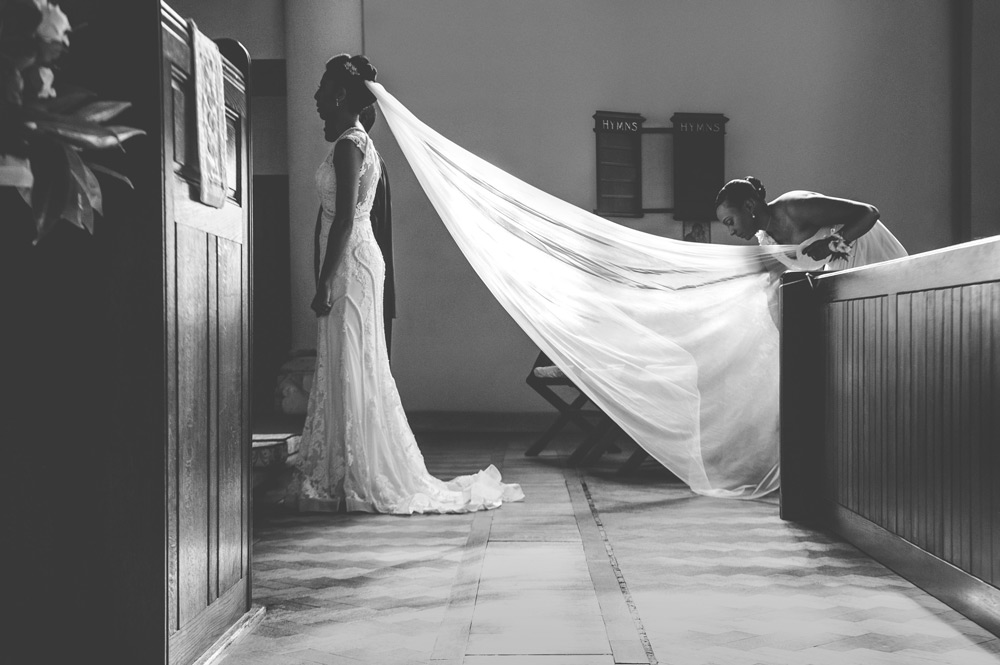 Maid of honour fixing bride&rsquo;s veil while the sun from the window illuminates it