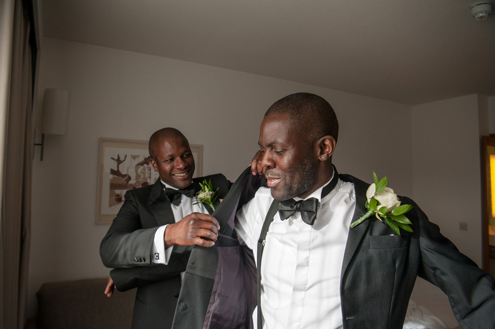 Best man helping groom into jacket
