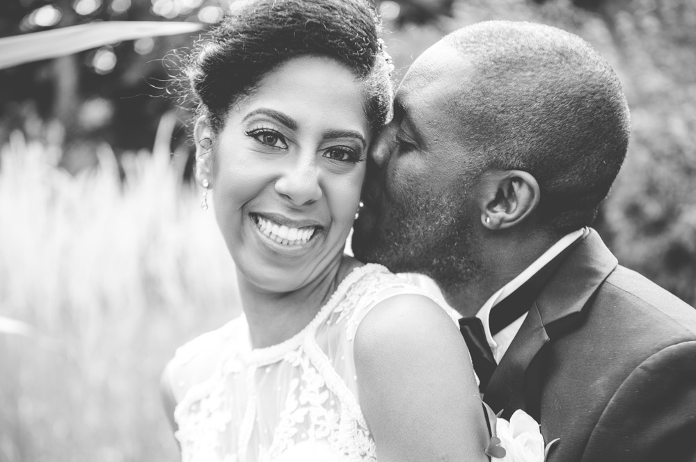 Groom kisses bride&rsquo;s cheek while she laughs at camera
