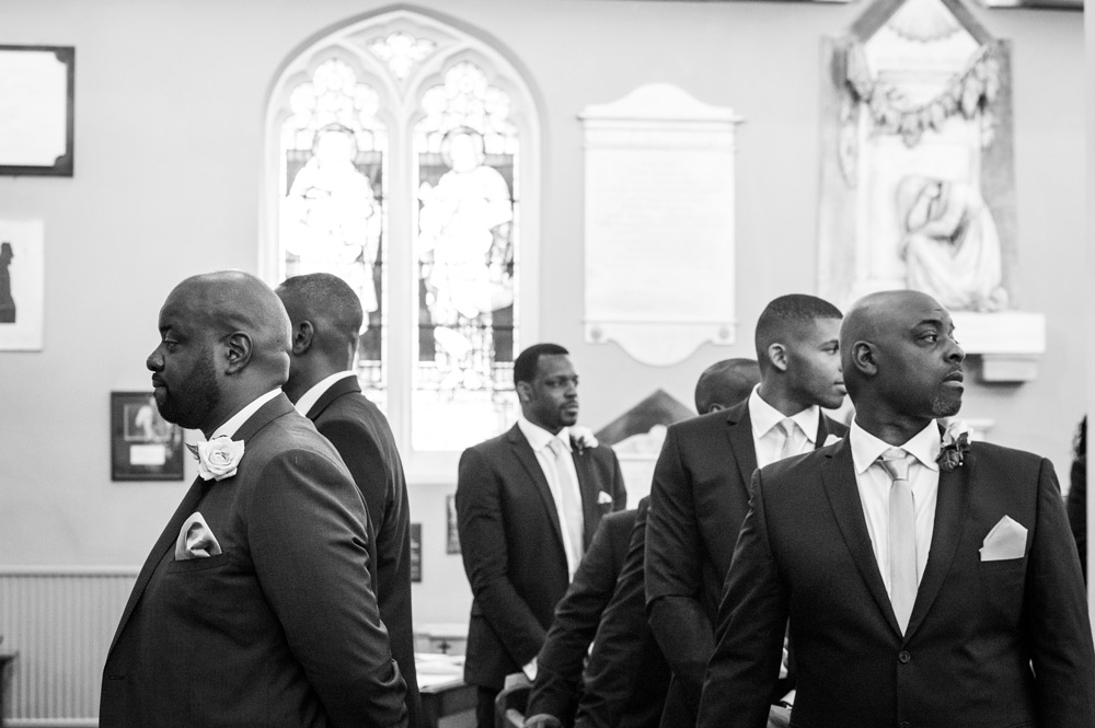Groom facing altar while groomsmen watch bride walk down the aisle