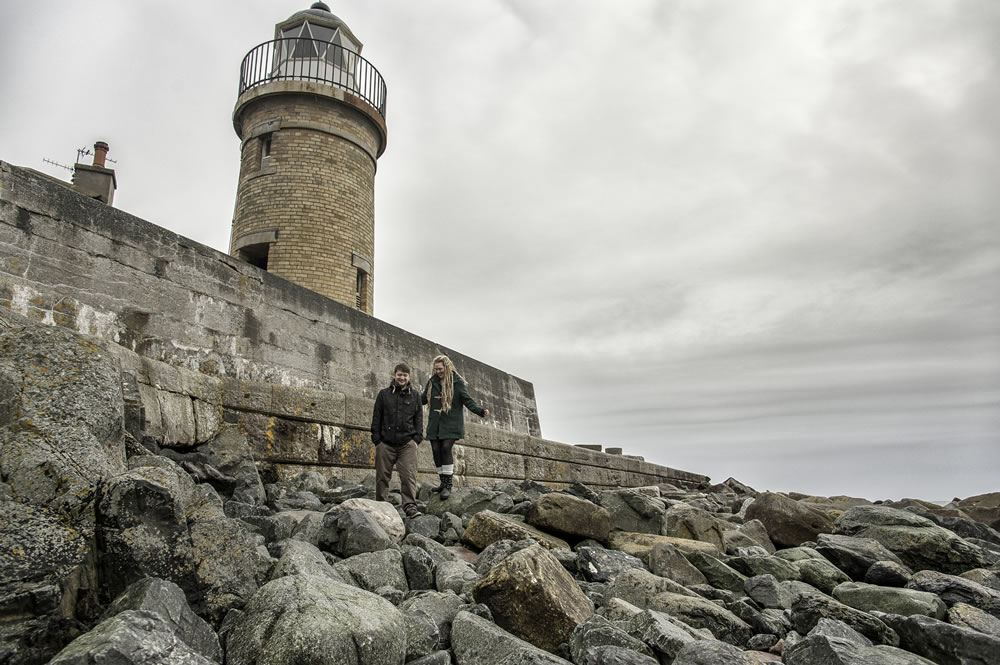 Couple walking on rocks near lighthouse