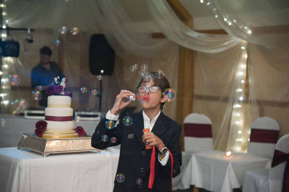 Boy blowing bubbles while stood in front of the wedding cake