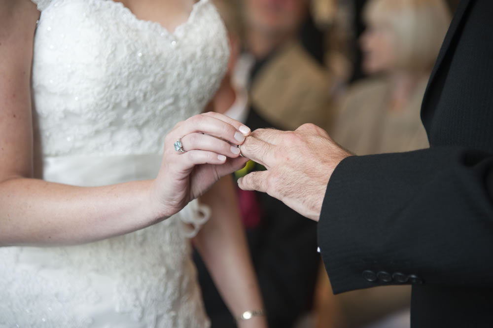 Bride putting ring on groom&rsquo;s finger